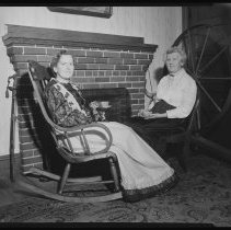 Two women next to a fireplace and spinning wheel