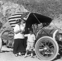 Mrs. Hetzel standing by the family car with her son and daughter. Sign on c