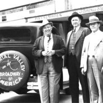 Three men standing between cars with signs on them that read Imperial Valle