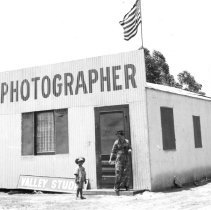 Mrs. Hetzel standing with son Leo in front of tin building that reads Photo