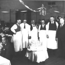 Elks Club birthday banquet / party. Men in aprons standing around a cake, p