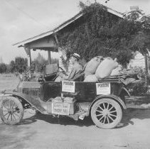 Man in parked car by house. The car is loaded with bags of poison.