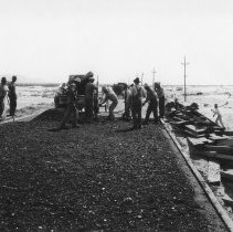 Dump truck dumping paving material, men smoothing out material.