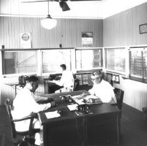 Interior of W.E. Whitacre Inc. packing shed office showing men at desks.