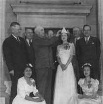 Six men standing behind three young women wearing white formal gowns.