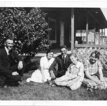 Group of two men and three women sitting in a yard.