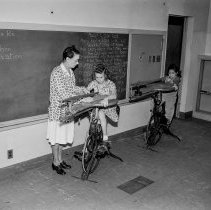 Washington Boulevard school, Elementary activities. Child on pedal saw being helped by teacher.