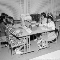 Class activities at Bellagio Road Elementary School.  Students and teachers are shown using the library facilities, music instruction, using audio visual equipment, playing musical instruments, and art.