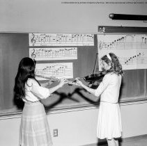 Class activities at Bellagio Road Elementary School.  Students and teachers are shown using the library facilities, music instruction, using audio visual equipment, playing musical instruments, and art.