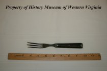 Fork with three long tines; it is made of pewter with a wooden handle.