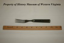 Fork with three long tines; it is made of pewter with a wooden handle.