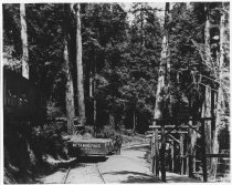 Gravity car by a cabin with residents on the porch, 1914-1928