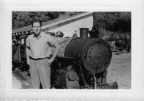 Man standing in front of a locomotive with a shed type building in backgrou