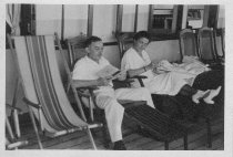 Man and woman sitting in what look like deck chairs on a ship, unknown