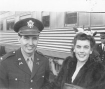 Military man and woman in front of train, unknown