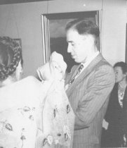 Man holding baby inside house, unknown.