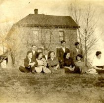 Unidentified men & women outdoors near brick structure