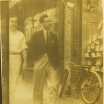 Two men walking down the street with a bicycle