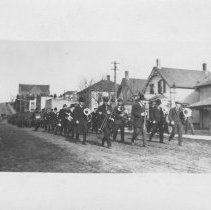 Brass band in civilian clothes marching on a dirt road in Wiarton, with wha