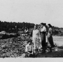 Four people on timber debris littered shoreline