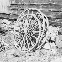 K-81-05-23 Buggy wheels standing beside old house.