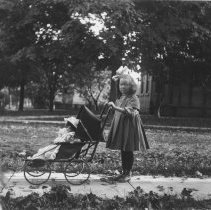 K-81-13-20 Unidentified little girl pushing a doll in a pram.