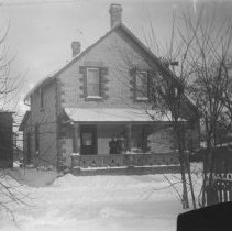 K-81-13-04 Adult and child on a snowy porch of a house in town.