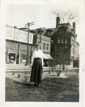 Sepia-toned image of a woman named Minnie in Clinton Park; behind her is the Westerman's Store, a hotel and the Detroit Medical College