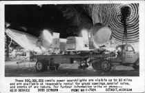 Black and white postcard depicting a truck with a trailer attacked to it and searchlights on the trailer