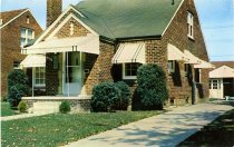 Color photographic postcard depicting a brick house with white awnings