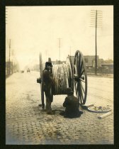 Sepia-toned photo showing two construction workers who are installing an underground electrical cable at a manhole