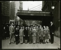 Sepia-toned enlargement of a photographic print depicting a group of safety patrol members posing with a trophy beneath the awning of the Statler Hotel on Bagley Street