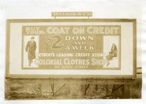 Black and white photographic print depicting a Walker & Co. billboard displaying an advertisement for Colonial Clothes Shop