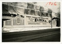 Black and white photographic print depicting a Walker & Co. billboard displaying an advertisement for Eureka vacuum cleaners