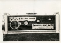 Black and white photographic print depicting a Walker & Co. billboard displaying an advertisement for the Enggass Jewelry Co.