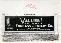 Black and white photographic print depicting a Walker & Co. billboard displaying an advertisement for the Enggass Jewelry Co.