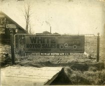 Black and white photographic print on fabric backing depicting a Michigan Highway Adv. Co. sign advertising White Motor Sales