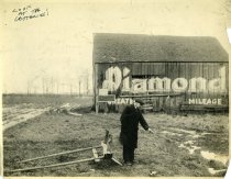 Black and white photographic print depicting a sign advertising Diamond Tires painted on the side of a barn