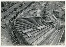 Digital scan of a black and white photo overlooking the construction of the Detroit-Windsor Tunnel within an excavated area on the site for the tunnel's Detroit terminal, as taken from a point above Bates Street facing northeast