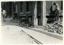 Digital scan of a sepia-toned photo taken of workers underpinning the southwest corner of a brick building at 232 Randolph Street as part of the construction of the Detroit-Windsor Tunnel