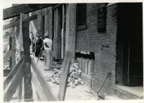 Digital scan of a sepia-toned photo taken of the underpinning put in place beneath the west wall of a brick building at 216 Randolph Street during the construction of the Detroit-Windsor Tunnel