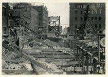 Digital scan of a sepia-toned photo taken overlooking the bracings for the excavation dug along Randolph Street during the construction of the Detroit-Windsor Tunnel, as taken from Woodbridge Street, facing south