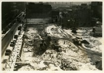 Digital scan of a sepia-toned photo overlooking the construction site for the Detroit terminal of the Detroit-Windsor Tunnel, as taken from a point above its northwest corner, near the intersection of Woodbridge Street and Bates Street, facing east