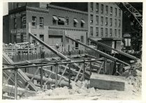 Digital scan of a sepia-toned photo of the excavation dug along Randolph Street, and the beams buttressing the west walls of the neighboring buildings along the east side of Randolph, between Franklin Street and Atwater Street, as taken from the northwest