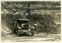 Digital scan of a sepia-toned photo of a steam shovel dumping chunks of clay into the bed of a truck within in an excavation on the construction site for the Detroit-Windsor Tunnel