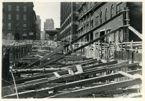 Digital scan of a sepia-toned photo of the bracing above the excavation for the Detroit-Windsor Tunnel through Randolph Street, and buttressing the western faces of the buildings along the east side of the street as taken facing north near Franklin Street