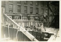 Digital scan of a sepia-toned photo of the underpinning on the eastern face of the brick building at 202 Randolph Street, put in place during the construction of the Detroit-Windsor Tunnel, as viewed from the northwest