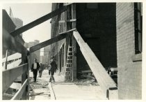 Digital scan of a sepia-toned photo of taken of beams buttressing the southwest corner of the building on the southeast corner of the Randolph Street and Woodbridge Street, as viewed from the sidewalk on the east side of Randolph facing north