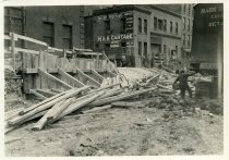 Digital scan of a sepia-toned photo of the bracing and ramp around the eastern edge of the construction site for the Detroit terminal of the Detroit-Windsor Tunnel along Randolph Street, at its intersection with Franklin Street, as viewed from the northwe