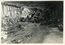 Digital scan of a sepia-toned photo of a steam shovel dumping chunks of clay into the bed of an International Harvester truck within an excavation at the construction site of the Detroit terminal of the Detroit-Windsor Tunnel